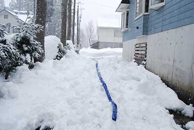 屋根から落ちた雪をポンプとホースを使って雪を消しています。